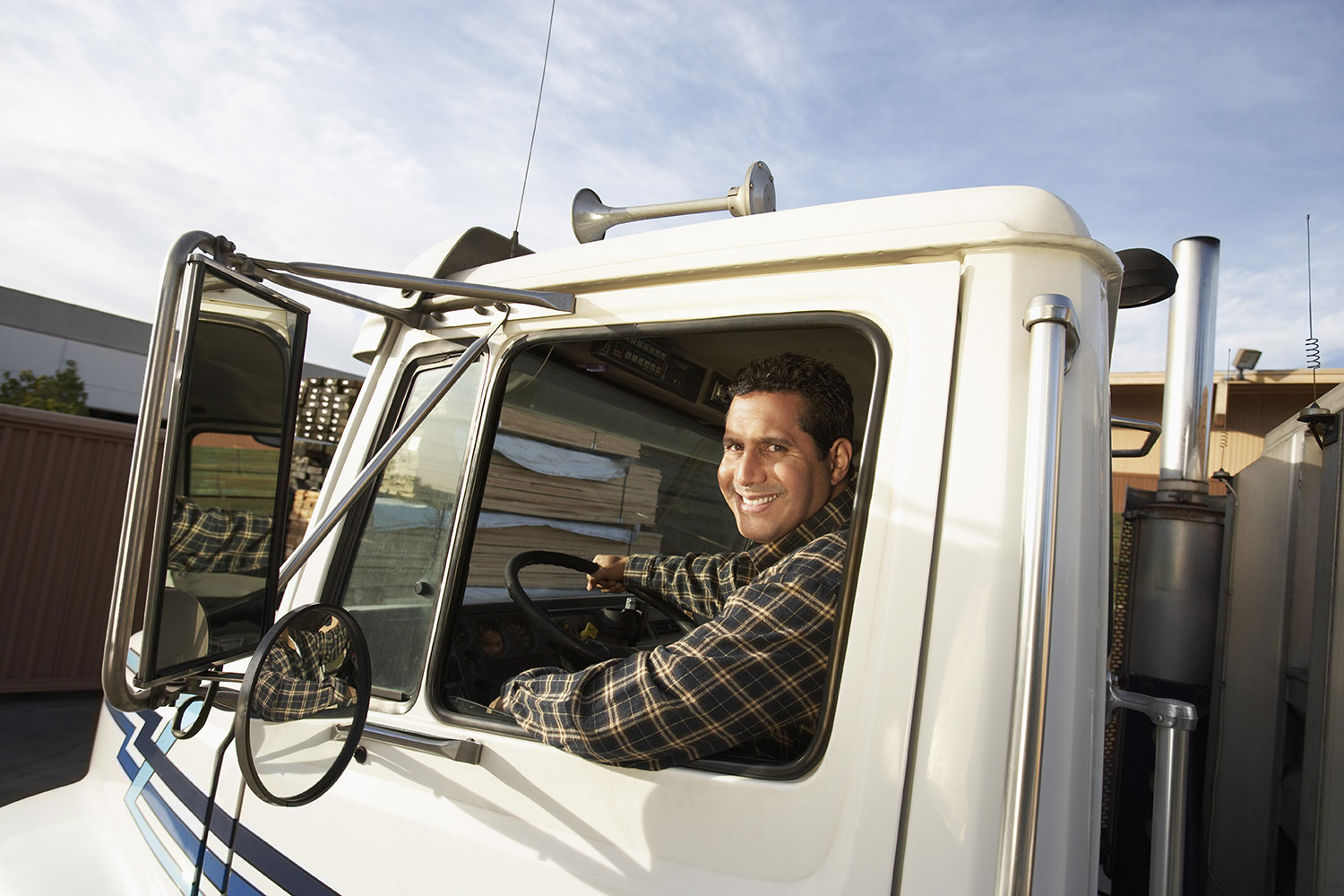 A smiling man inside the cab of a 16-wheeler truck