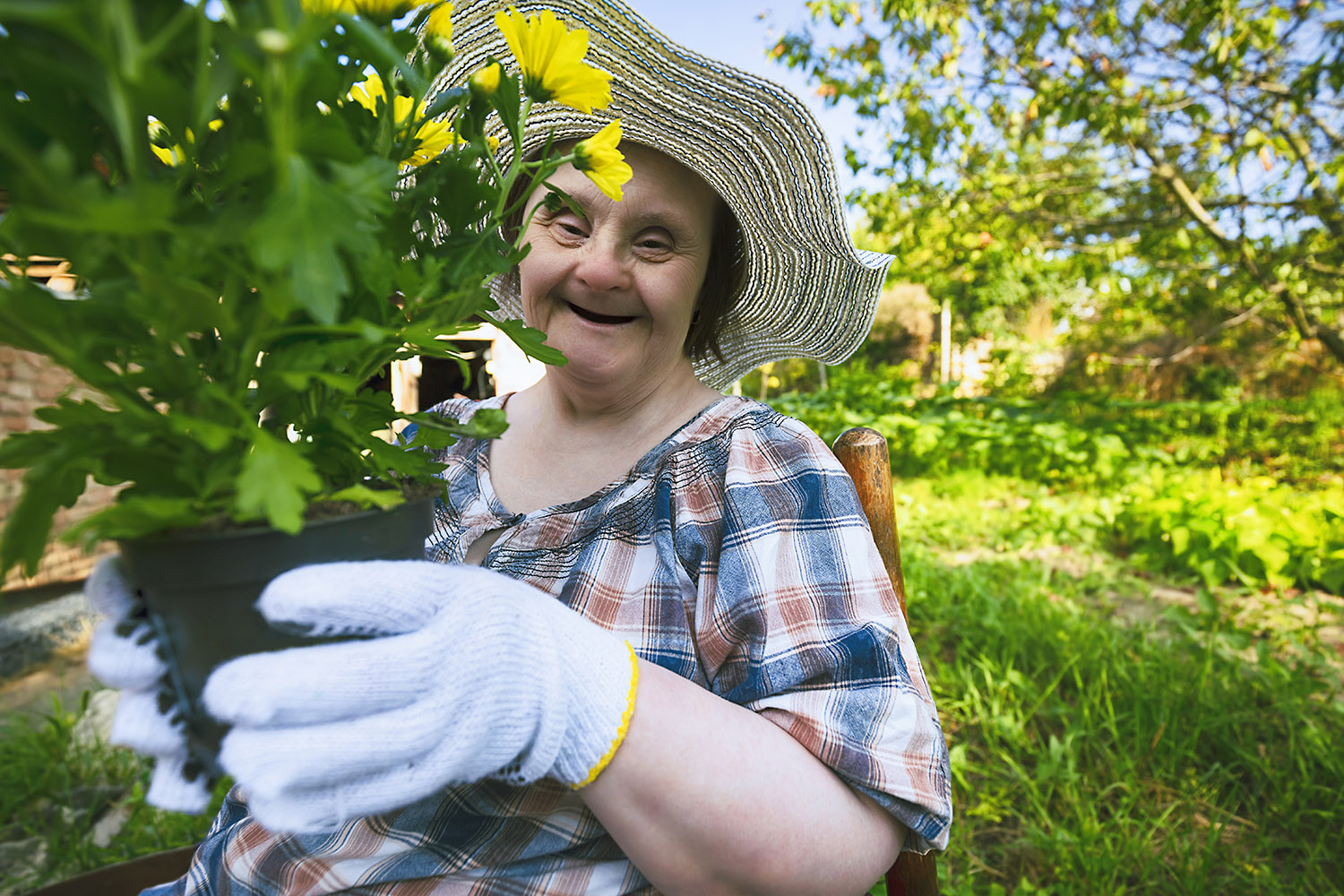 A woman living with down syndrome is working in the garden and holding a pot with flowers